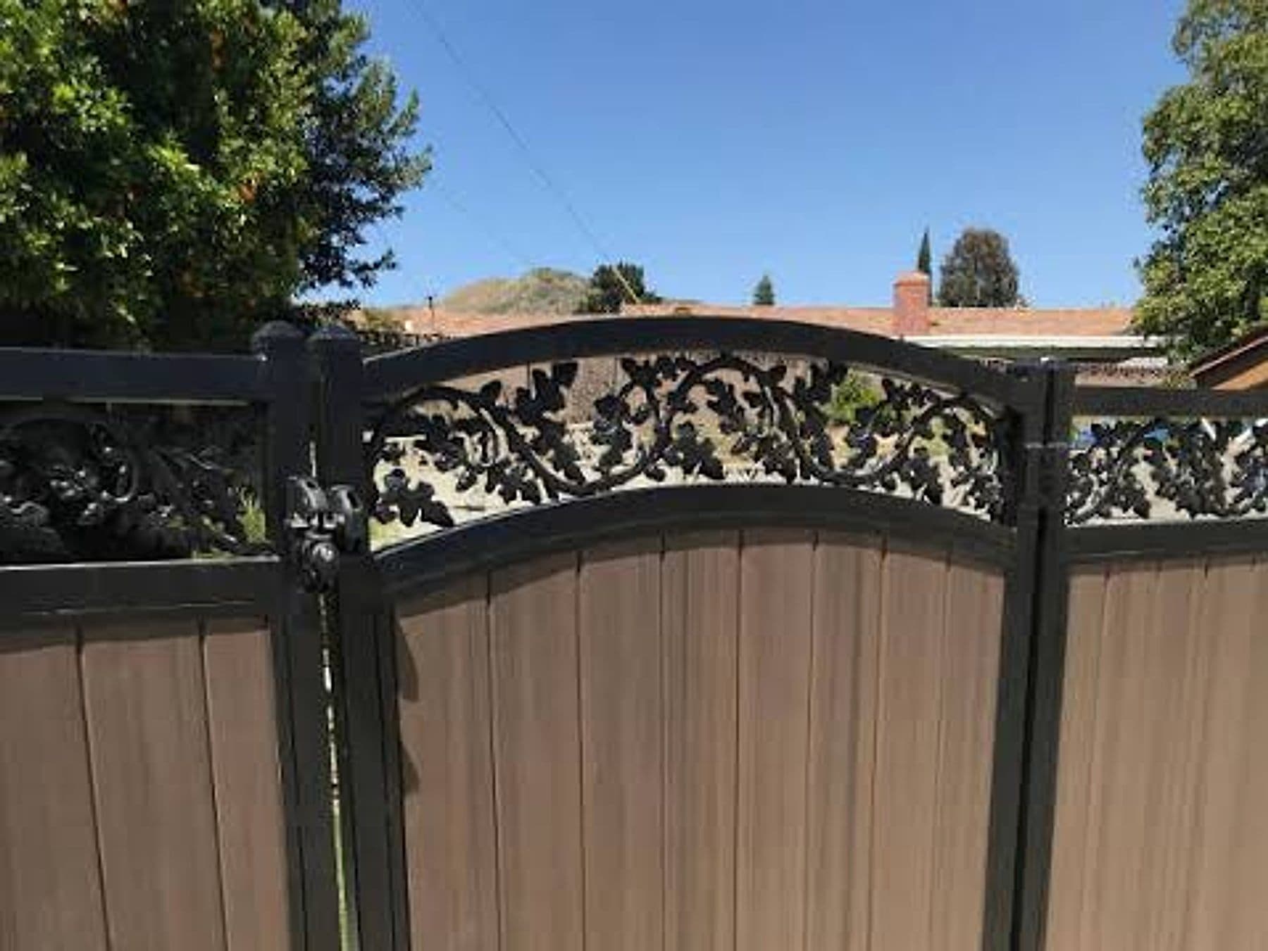 Wood privacy fence with a decorative wrought-iron gate under a tree