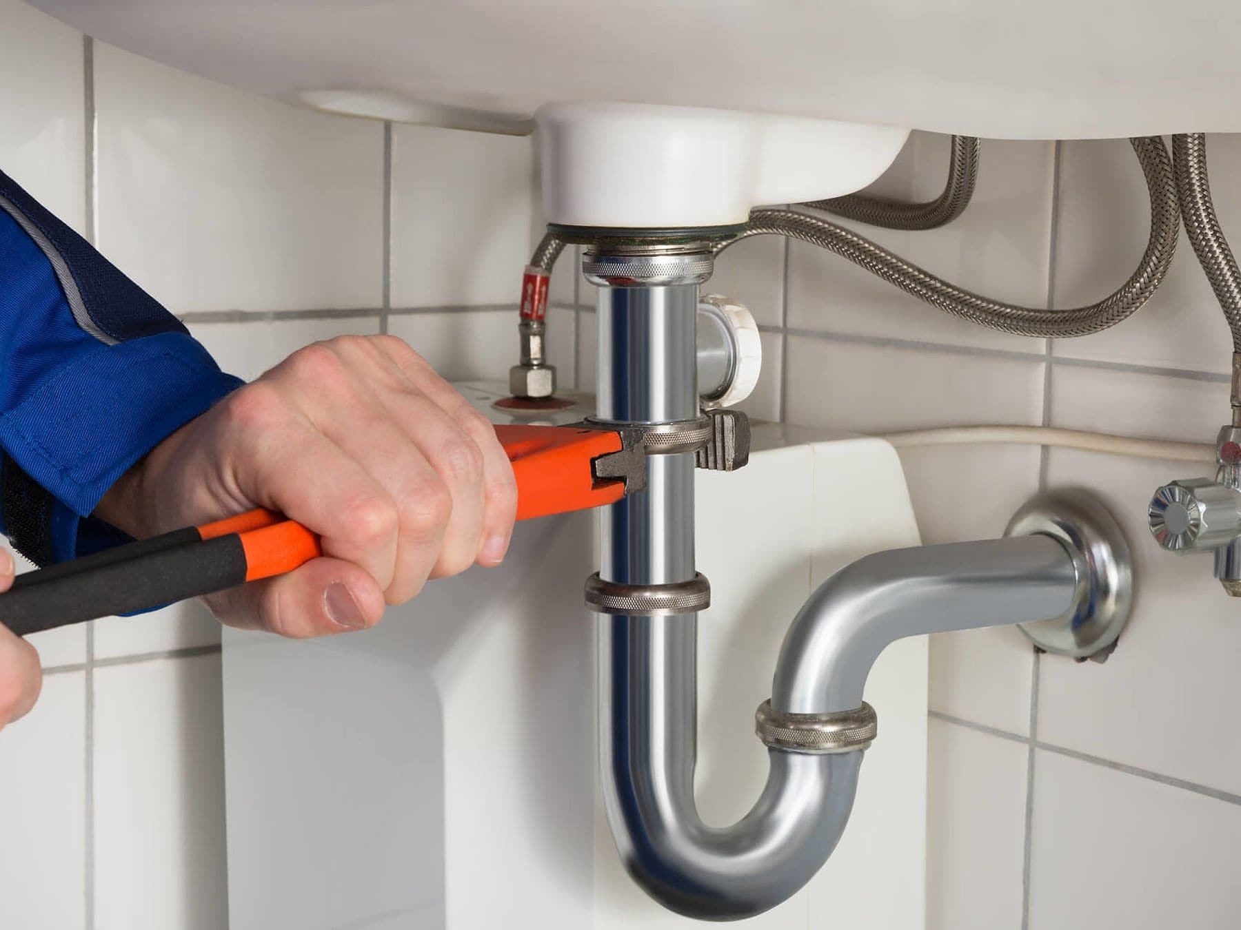Plumber tightening a chrome sink drain with a wrench under a bathroom basin