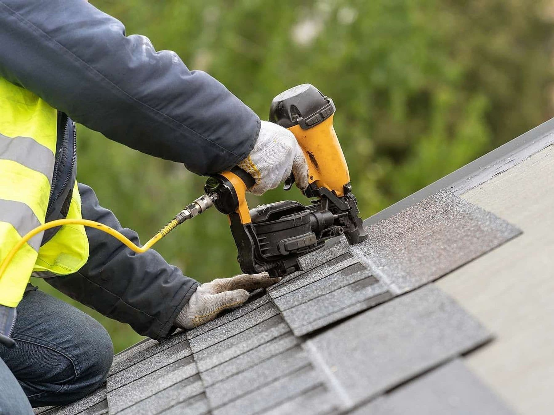 Roofer nailing asphalt shingles with a pneumatic nail gun
