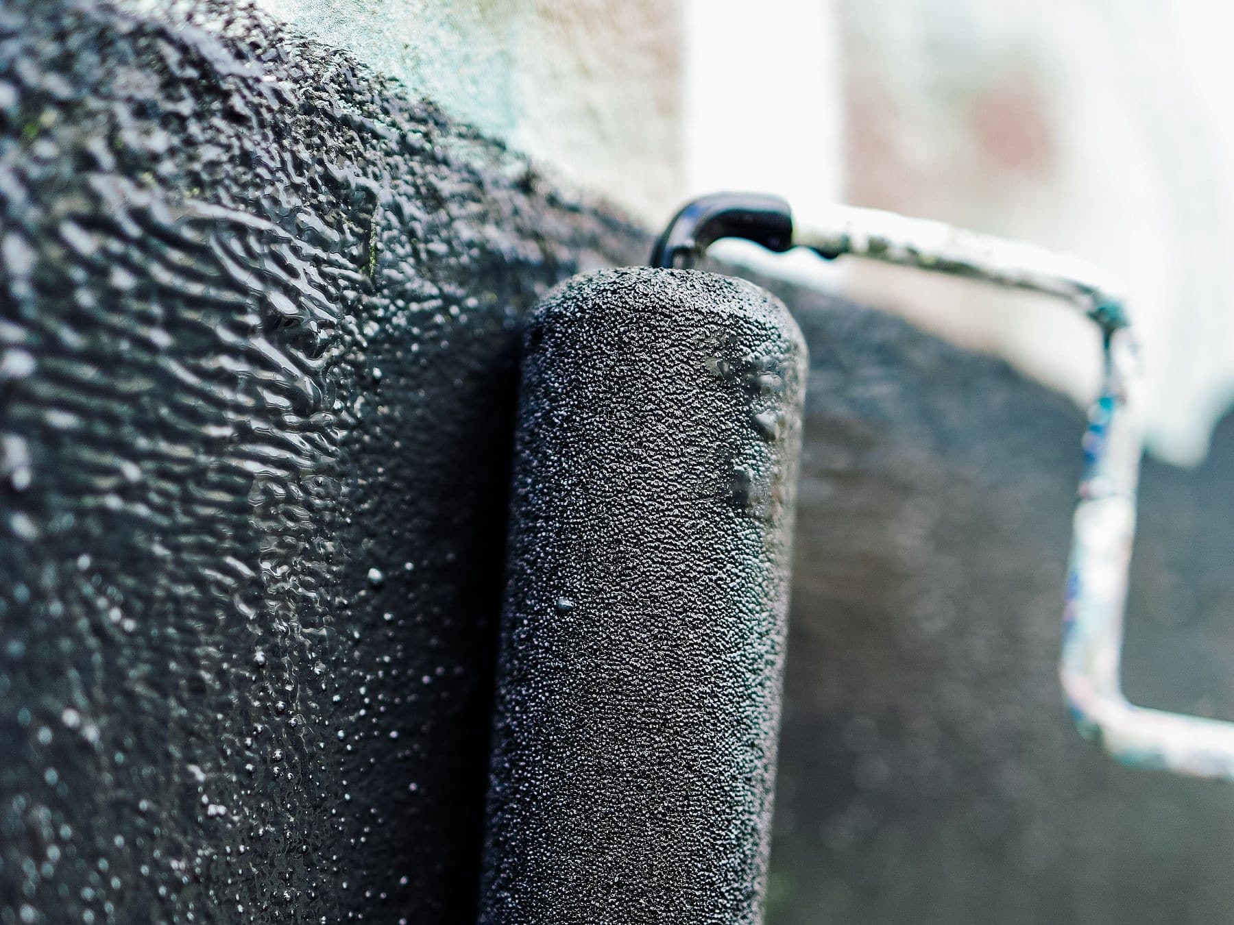 Roller applying grey waterproofing coating to a wet concrete surface